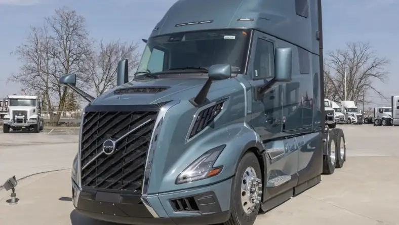 Front view of a grey Volvo semi-truck in a commercial vehicle yard with other trucks in the background