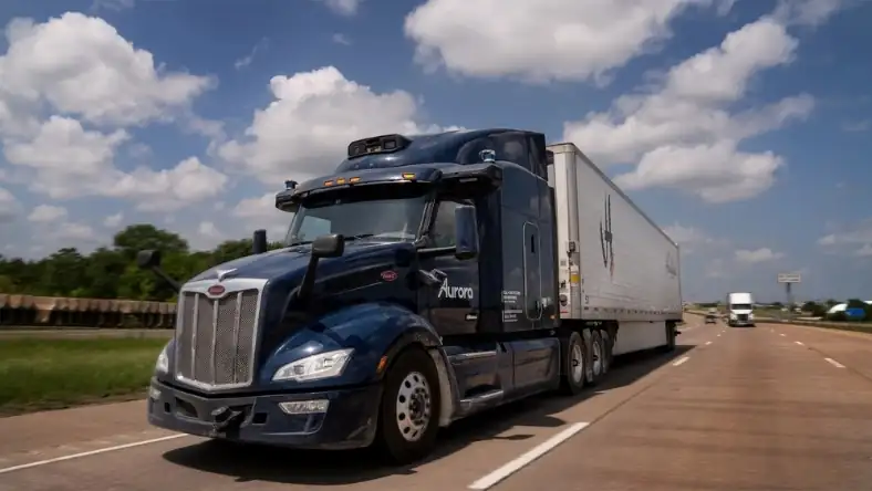 Dark blue autonomous semi-truck with Aurora branding and rooftop sensor array traveling on a Texas highway